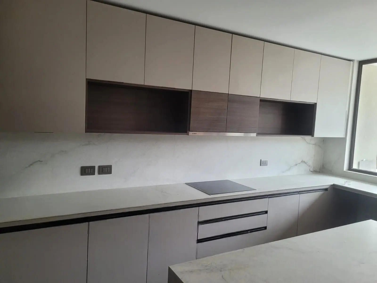 Cocina moderna fabricada en melamina en Chile con gabinetes claros, detalles en madera oscura y cubierta de cuarzo marmolado blanco con vetas grises