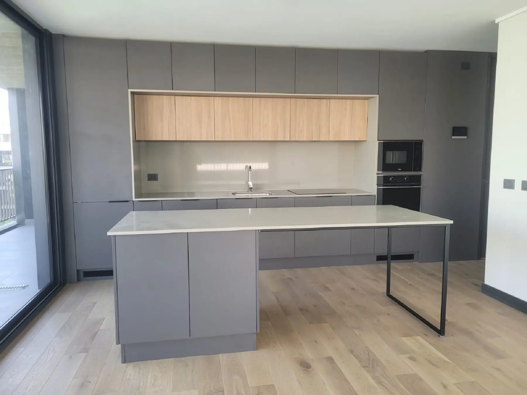 Cocina moderna fabricada en melamina en Chile con gabinetes gris mate, muebles superiores en madera clara y cubierta de cuarzo con isla amplia