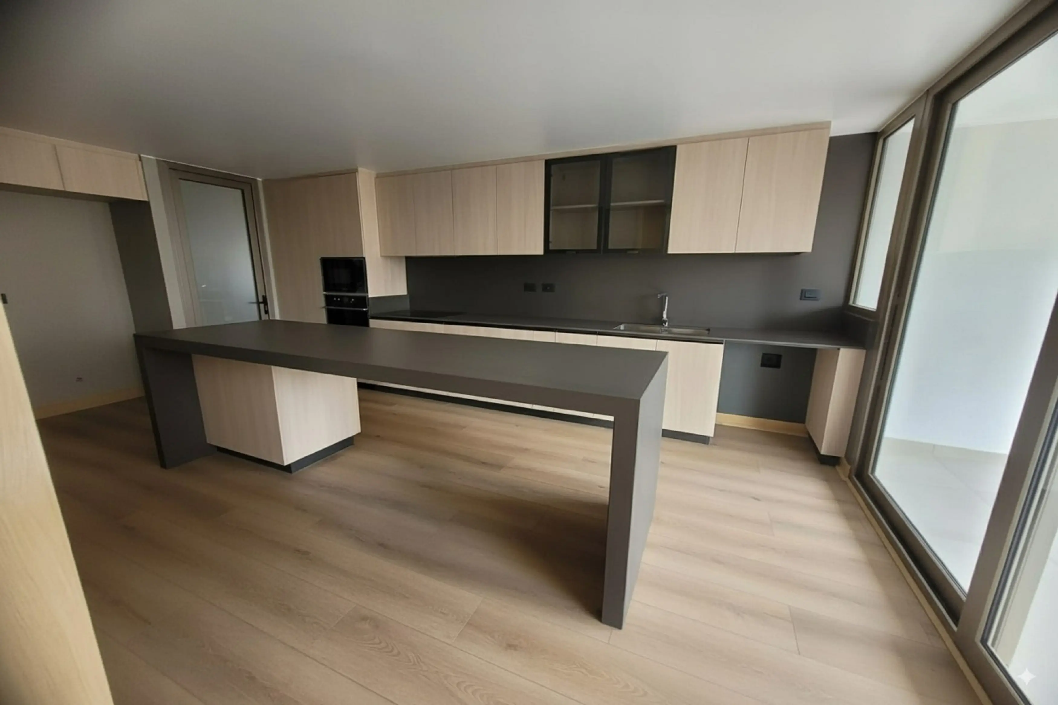 Cocina moderna fabricada en melamina en Chile con gabinetes de madera clara, cubierta de cuarzo oscuro y barra funcional con luz natural