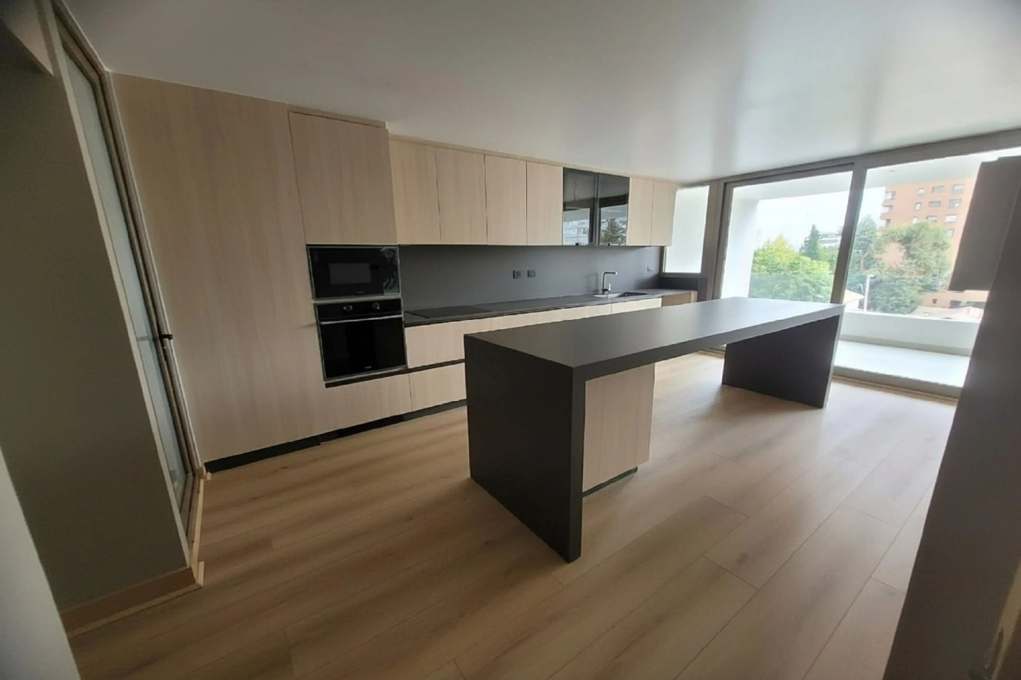 Cocina moderna fabricada en melamina en Chile con gabinetes de madera clara, cubierta de cuarzo negro y diseño luminoso con isla amplia