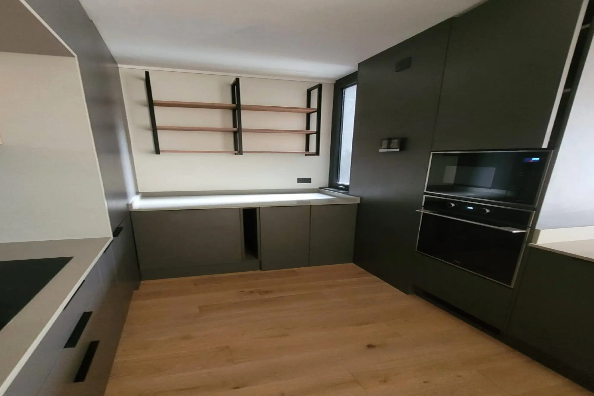 Cocina moderna en melamina negra con horno empotrado, repisas de madera y cubierta blanca, diseño de Style Muebles en proceso de instalación